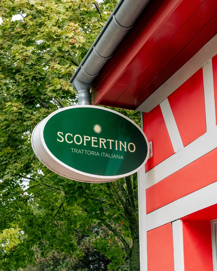Enseigne ovale verte « Scopertino, Trattoria italiana » sur la façade rouge