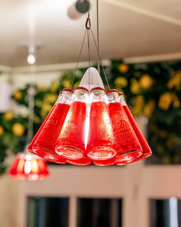 Lustre fait de bouteilles de Campari Soda devant le papier peint aux citrons